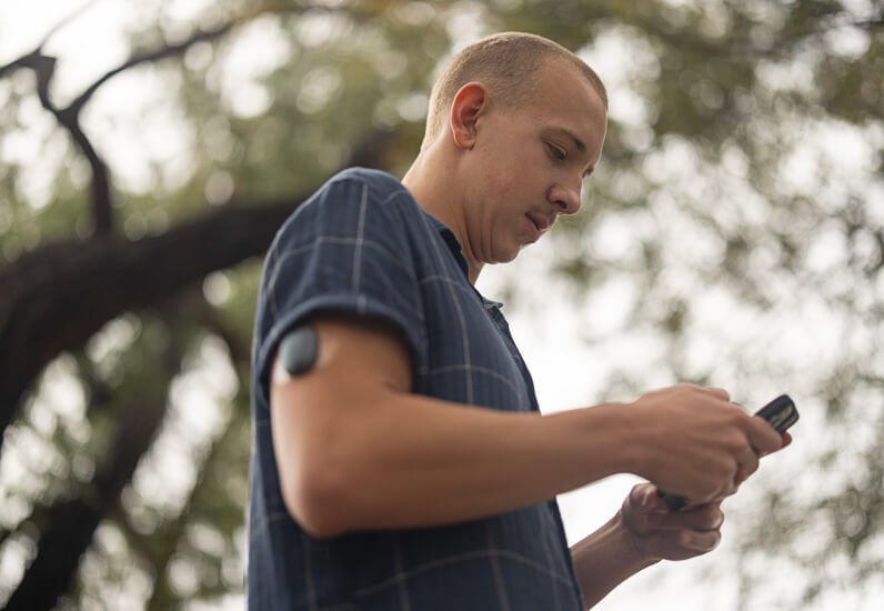 Ung man ser på sin mobiltelefon med en Eversense-sändare på armen