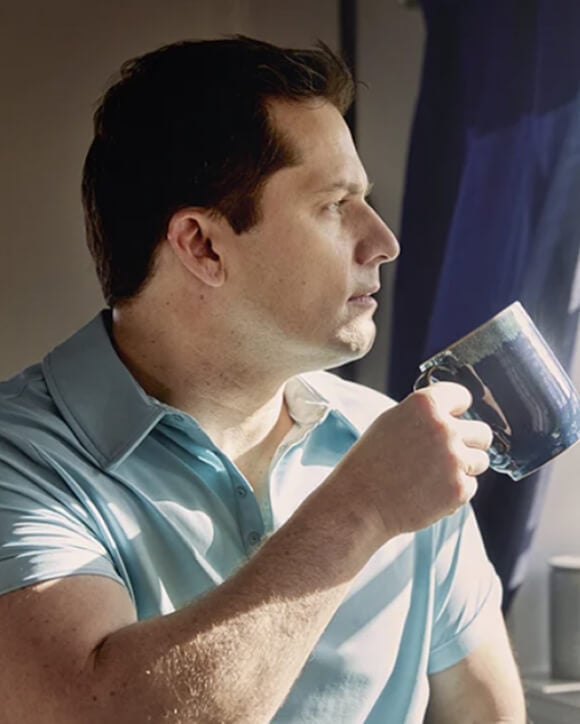 En Eversense CGM-användare som håller en blå mugg och använder Eversense-smartsändaren på armen