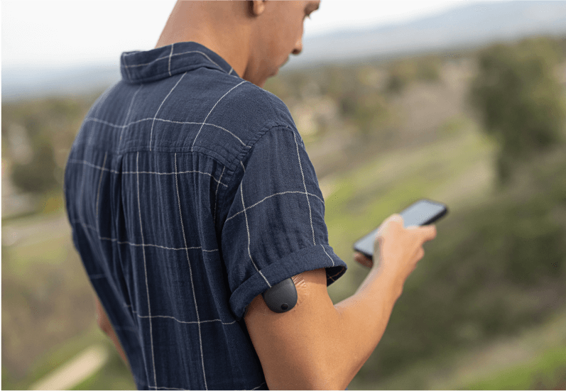 Eversense-användare som står utanför och använder en smartphone för att övervaka sina glukosmönster 