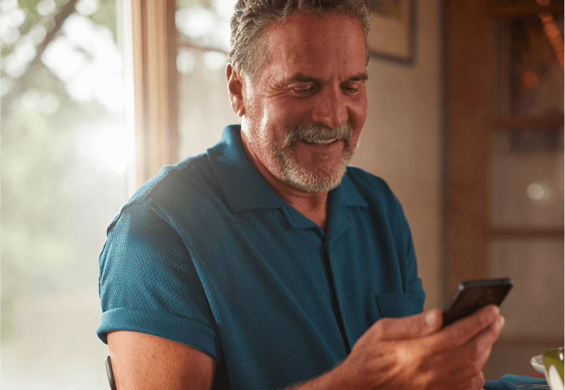 En medelålders man ser sina glukosvärden på sin mobiltelefon med Eversense-sändare på armen