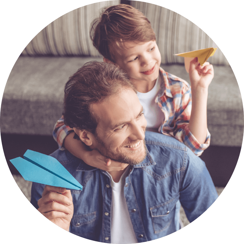 En Eversense CGM-användare håller ett blått pappersflygplan och ler, med ett barn på ryggen som håller ett gult flygplan.