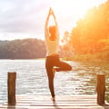 Eversense-användare som gör yoga-trädposition på en träbrygga, omgiven av en lugn sjö och skogsklädda kullar, med solljus.