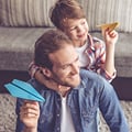 En Eversense CGM-användare håller ett blått pappersflygplan och ler, med ett barn på ryggen som håller ett gult flygplan.