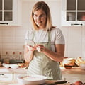 Eversense CGM-användare i ett förkläde använder en smartphone i ett ljust kök, med bakingredienser på bänken.