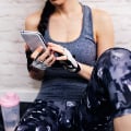 Eversense-användare som håller smartphone, iklädd träningskläder och fingerlösa handskar, sitter inomhus mot en vit tegelvägg.