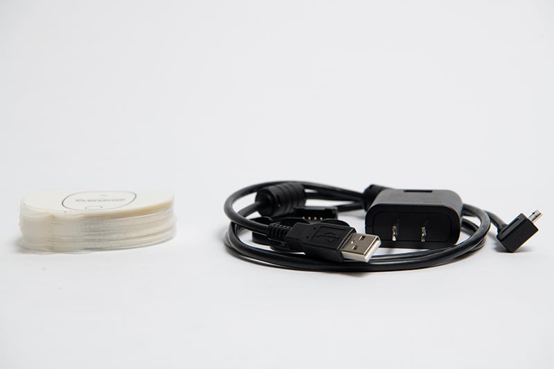 En USB-laddningskabel med adapter ligger ihoprullad på en plan yta bredvid sändarplåster
